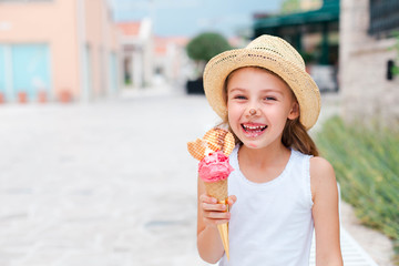 Funny kid is eating ice cream. Child is enjoying melting italian gelato. Happy cute girl in straw hat is laughing and tasting delicious street food in summer vacation. Lifestyle moments of childhood.