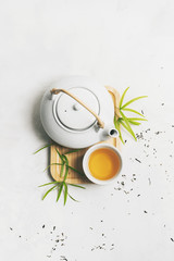 Asian tea concept with Tea set on bamboo mat surrounded with dry green tea on white background with copy space. Brewing and Drinking tea.