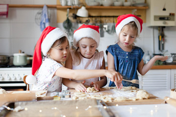 Children are cooking Christmas cookies in cozy home kitchen. Cute kids in santa hats preparation holiday dinner for family. Three sisters bake Xmas biscuits. Lifestyle moments. Children chef concept.