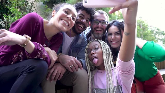 Black woman in braids takes a selfie with friends. Smiles, grimaces and fun. Multiethnic brazilian people having a break for a selfie photograph all together in the outdoor. Diversity and friendship