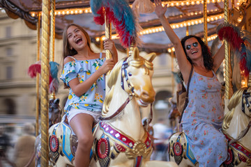 Obraz na płótnie Canvas Happy family (mother and daughter) at the carousel. Merry go round horse with colorful lights 