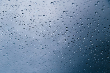 Close up of rain drops on the windshield, front window of a car on a blue gray background of dark...