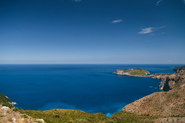 Fototapeta premium A top view at dark blue Ionian Sea, Asos village and Assos peninsula from a road. Aerial view, summer scenery of famous and extremely popular travel destination in Cephalonia, Greece, Europe.