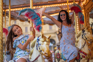 Fototapeta na wymiar Happy family (mother and daughter) at the carousel. Merry go round horse with colorful lights 