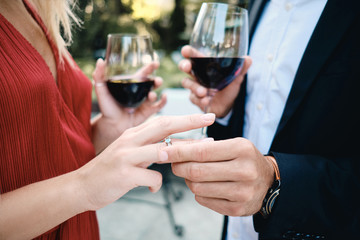 Close up young couple with glasses of red wine putting on wedding ring in restaurant outdoor