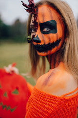 Young blonde girl with halloween face art posing outdoor.  Helloween celebration concept.