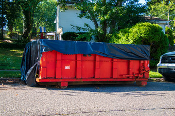 Red dumpster with black plastic liner on a asphalt street near the side of a house