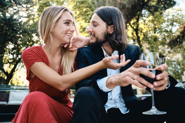 Young beautiful couple with glass of wine happily looking at each other and talking on date in restaurant outdoor