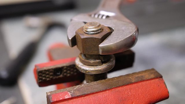 Loosening rusty nut using an adjustable crescent wrench and vise. Repairman using spanner wrench and clamp to remove nut from bolt.