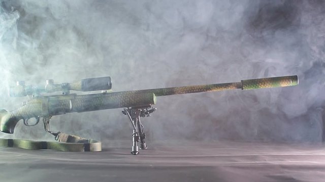 Slow plan of sniper rifle with silencer. Dark background and overhead light.