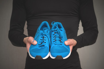 Pair of new sneakers in the sportsmen hands on gray background.