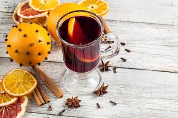 Glass of delicious mulled wine with oranges anise cinnamon on white wooden table