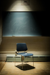 Portrait of an Empty School Chair in a Dark, Shadowy Classroom - in Front of a Chalkboard with a...