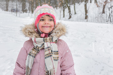 Fototapeta na wymiar Outdoor winter portrait of a little girl in a snowy day in the park. Golden hour, active lifestyle.