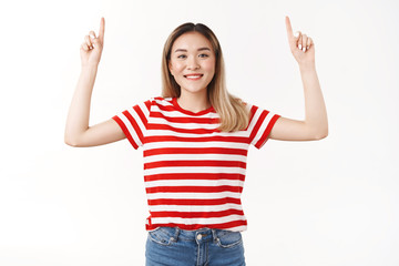 Cheerful upbeat positive asian teenage girl raise hands up proudly showing promo index fingers pointing upwards smiling delghted confidently recommend good product, standing white background