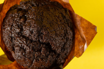 Chocolate muffin in paper on a yellow background