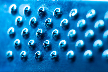 Metal surface with holes close-up in blue light, abstract background.