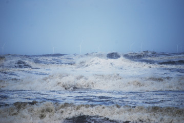 Storm at sea, coastline/beach The Netherlands, with windmills