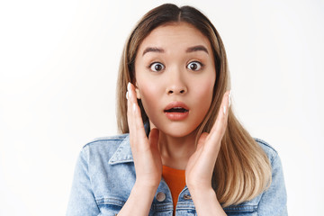 Headshot shocked surprised blond asian girl pop eyes stare camera impressed wondered touch face...