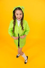 Easy fastening. Happy schoolgirl going out on yellow background. Small schoolgirl dressing raincoat and hood for rainy day. Little schoolgirl feeling protected for autumn weather