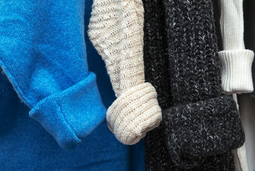 warm multi-colored knitted sweaters hang on wooden trempels