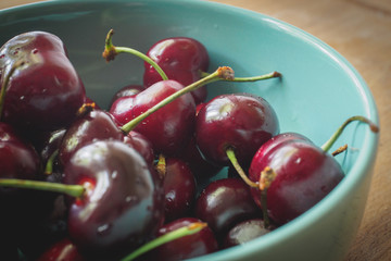 Vintage looking image of a light blue bowl full of red cherries on a wooden board. Landscape format.