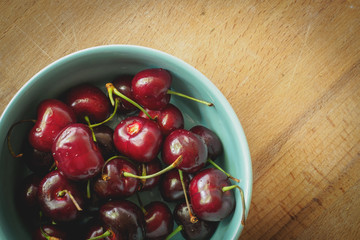 Vintage looking image of a light blue bowl full of red cherries on a wooden board. Landscape format.