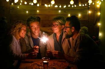 Happy family of four people sparkling wishing a wonderful new year 2020. Large pizza on the wooden table. Multi generation. Concept of happiness and love in a dark night