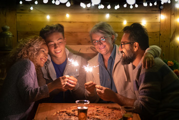 Happy family of four people sparkling wishing a wonderful new year 2020. Large pizza on the wooden table. Multi generation. Concept of happiness and love
