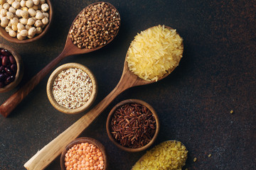 Various organic cereals and grains in wooden spoons and bowls on dark stone background