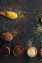 Various organic cereals and grains in wooden spoons and bowls on dark stone background