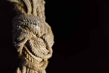 Closeup of a complicated, undetachable knot of hemp rope against a dark background