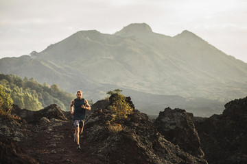 Young athlete man trail running in mountains in the morning. Amazing volcanic landscape of Bali mount Batur on background. Healthy lifestyle concept. - 291368199
