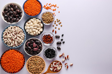 Red and brown lentils, black, brown and white beans are legumes that contain a lot of protein are located in bowls on white background, concept is healthy eating, copy space