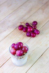 GLASS WITH YOGURT DESSERT WITH CEREALS, NUTS AND GRAPES ON WOODEN TABLE