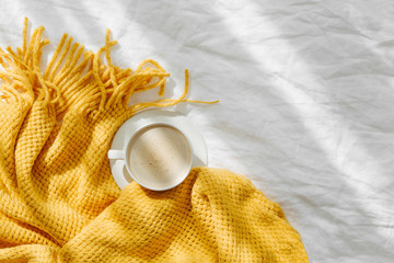 Bedding with a yellow knitted plaid and cup of coffee . Cozy background with copy space. Hygge concept.