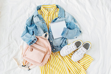 Blue jean jacket and Yellow dress  with backpack, book and sneakers on white. Women's stylish...