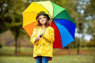 Happy funny child girl with multicolor umbrella in rubber boots at autumn park
