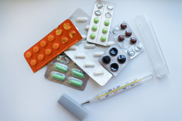 A close-up of pills in different packages on a white surface and a mercury thermometer