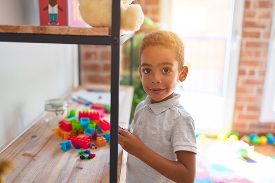Beautiful african american toddler standing playing with small building blocks on shelving at kindergarten