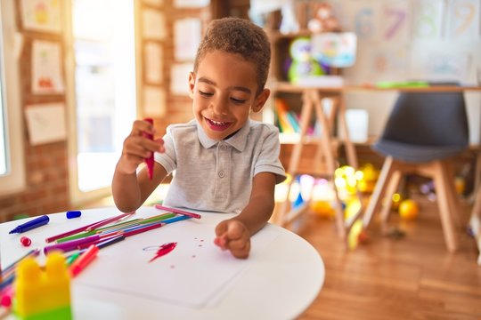 Beautiful african american toddler drawing using paper and marker pen smiling at kindergarten