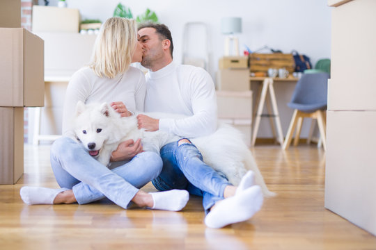Young beautiful couple with dog kissing sitting on the floor at new home around cardboard boxes