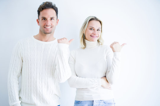Young beautiful couple wearing casual t-shirt standing over isolated white background smiling with happy face looking and pointing to the side with thumb up.