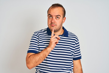 Young man wearing casual striped polo standing over isolated white background Thinking concentrated about doubt with finger on chin and looking up wondering