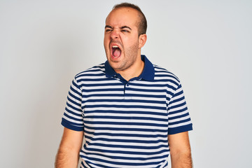 Young man wearing casual striped polo standing over isolated white background angry and mad screaming frustrated and furious, shouting with anger. Rage and aggressive concept.