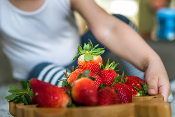 baby boy hands touch and take raw fresh strawberries on wooden bamboo plate indoor. baby exploring fruit