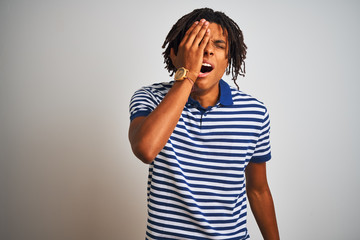 Afro man with dreadlocks wearing striped blue polo standing over isolated white background Yawning tired covering half face, eye and mouth with hand. Face hurts in pain.