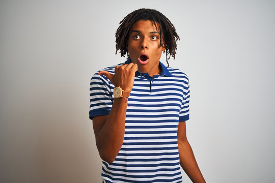 Afro man with dreadlocks wearing striped blue polo standing over isolated white background Surprised pointing with hand finger to the side, open mouth amazed expression.