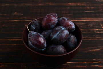 Fresh appetizing plums in a brown bowl, summer concept, copy space.