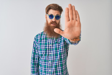 Young redhead irish man wearing casual shirt and sunglasses over isolated white background doing stop sing with palm of the hand. Warning expression with negative and serious gesture on the face.